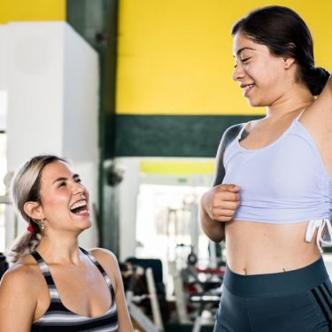 Two women in activewear sharing a joyful moment during a gym workout session.