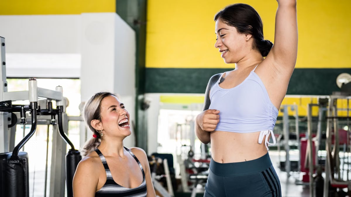 Two women in activewear sharing a joyful moment during a gym workout session.